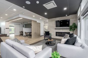 A modern living room with a grey sofa, a black coffee table, and a fireplace with a TV above it.